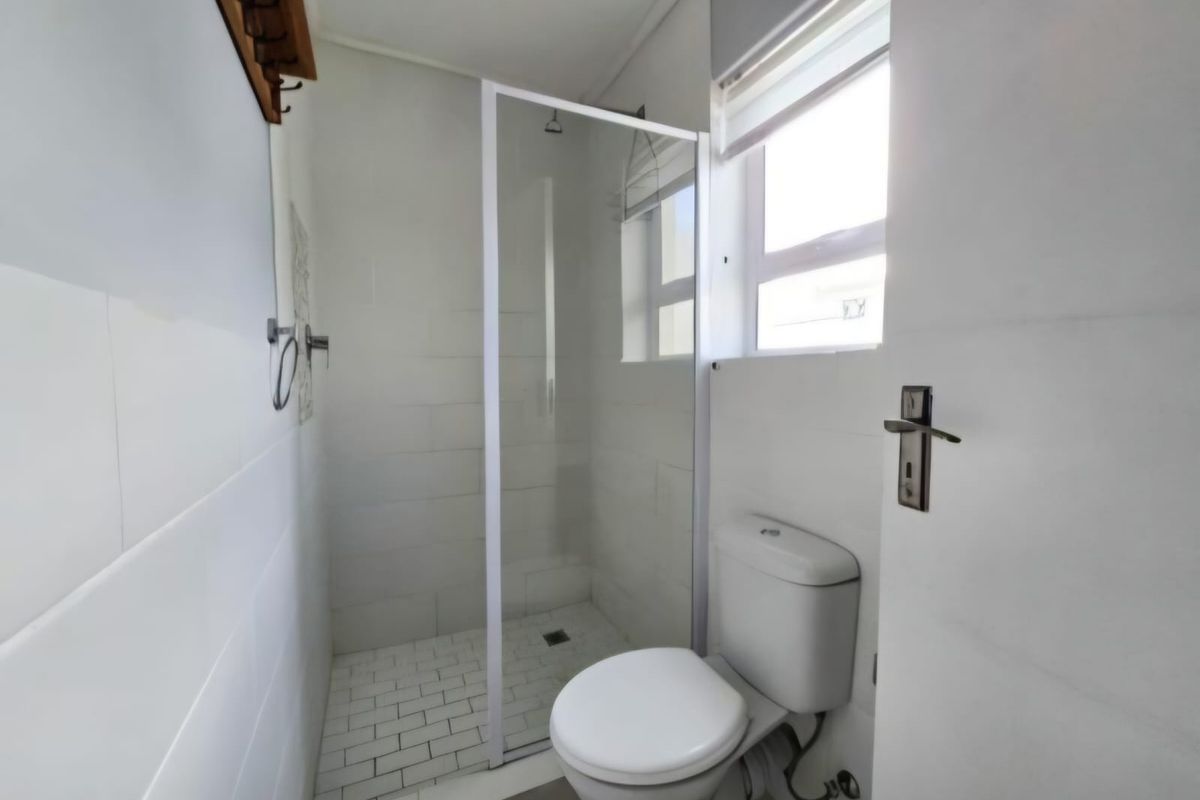 A clean, modern bathroom featuring a glass-enclosed shower, white tiled walls, and a standard toilet.