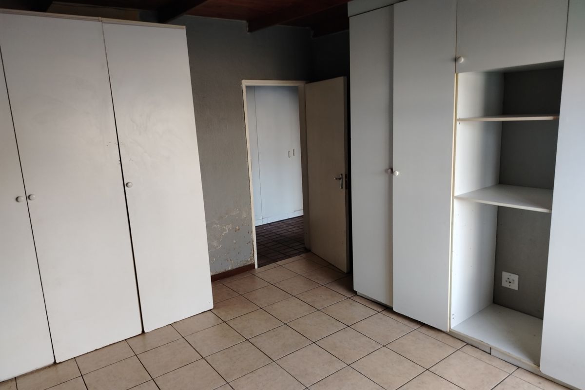 Bedroom featuring built-in cupboards, tiled flooring, and a timber-paneled ceiling, with an adjacent doorway leading to another room.