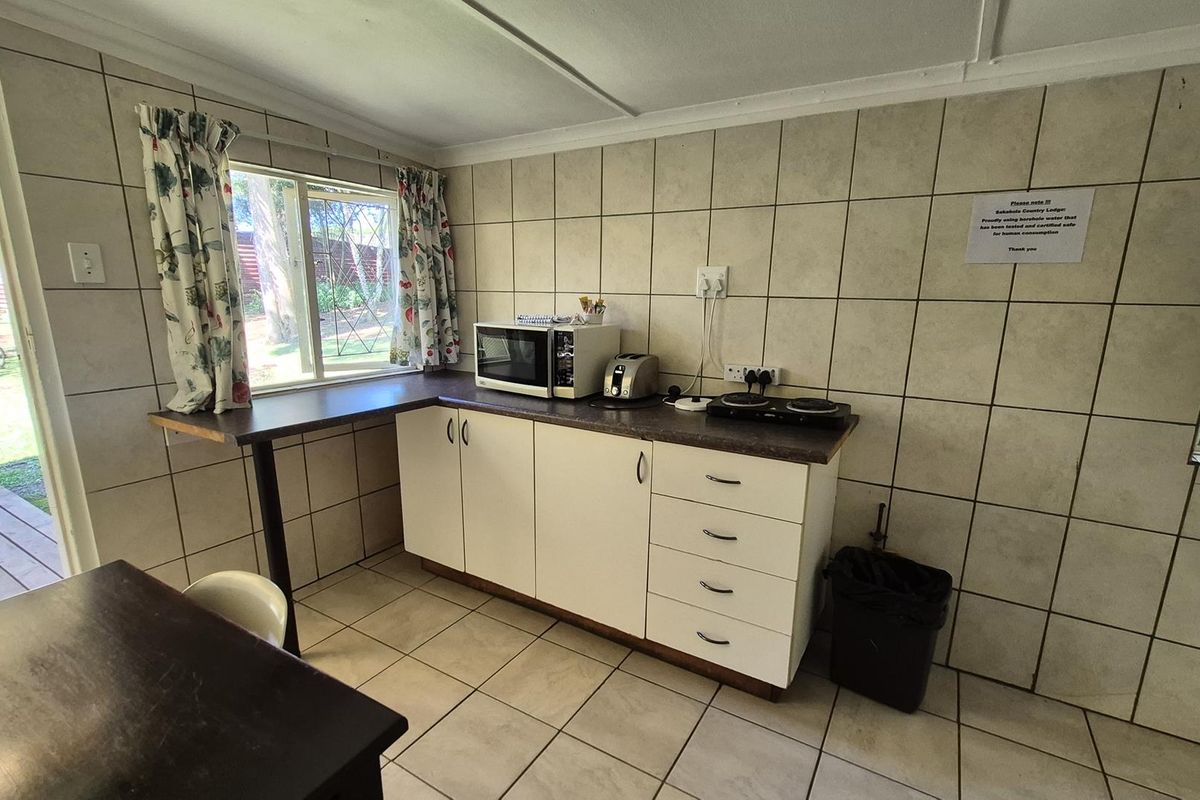 A compact kitchen area featuring tiled walls, built-in cabinetry with laminate countertops, and a built-in electric hob, with direct access to an outdoor patio.