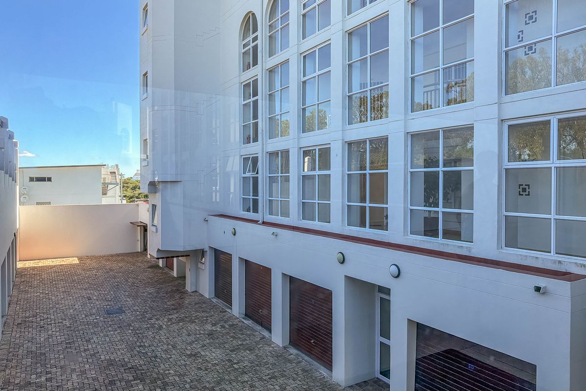 Rear exterior view of the apartment building featuring a paved courtyard area and multiple ground-level garage access points.