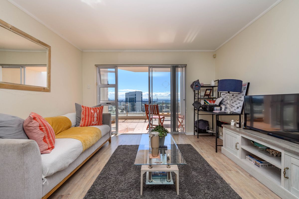 A bright living room featuring laminate flooring and a large sliding glass door providing access to a balcony with city views.