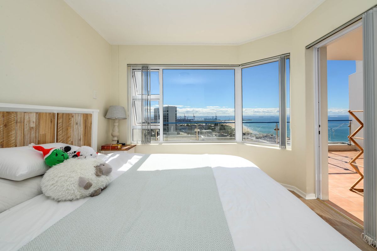Bright bedroom featuring a large bay window with expansive ocean and city views, plus direct access to a private balcony.