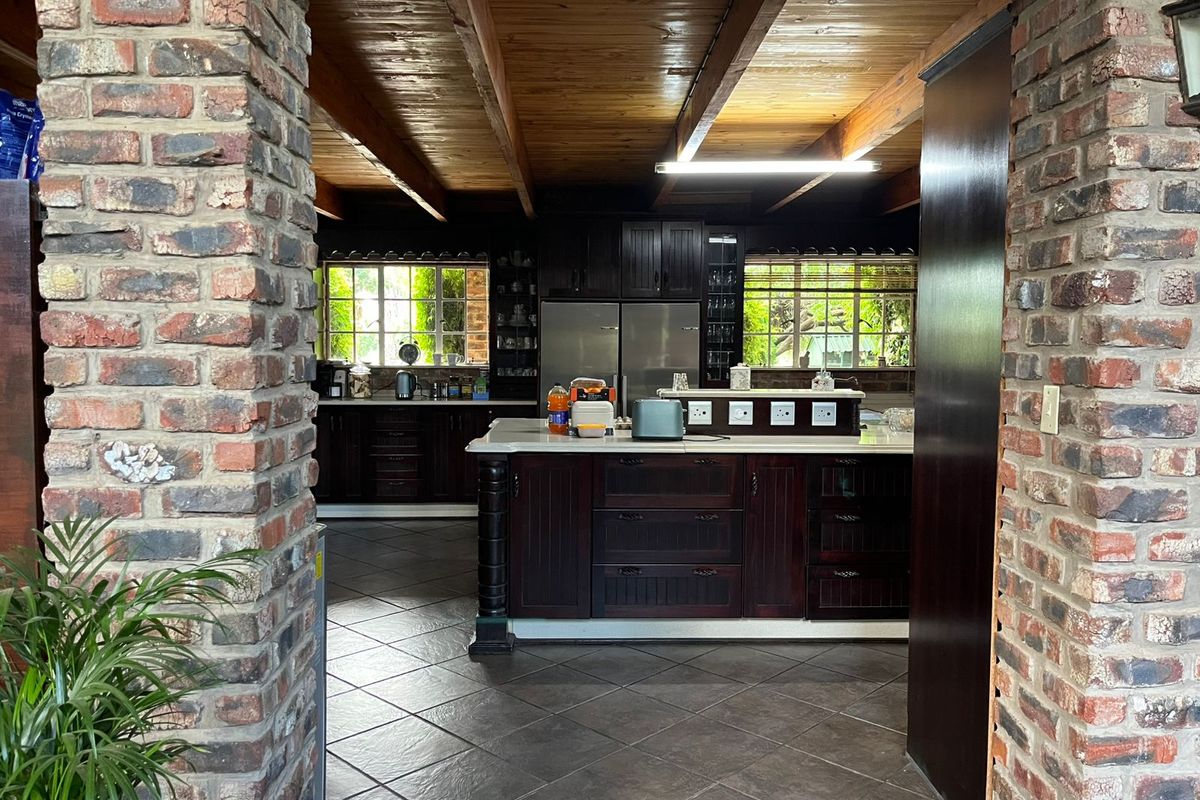 Spacious kitchen featuring dark wood cabinetry, a central island, exposed timber ceiling beams, and rustic brick pillars, offering a warm and traditional aesthetic.