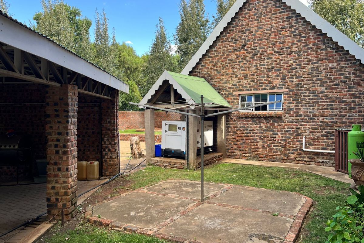 Rear exterior view of a face-brick building featuring a covered generator housing area and a paved patio space in a garden setting.