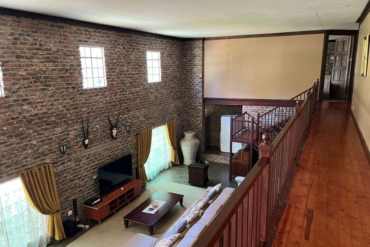 Spacious double-volume living area featuring exposed brick walls, wooden flooring, and a mezzanine walkway with a wooden balustrade overlooking the main lounge.