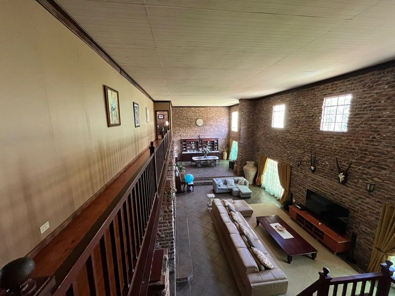 Spacious open-plan living area featuring double-volume ceilings, exposed brick walls, and a mezzanine level overlooking the main lounge and dining space.