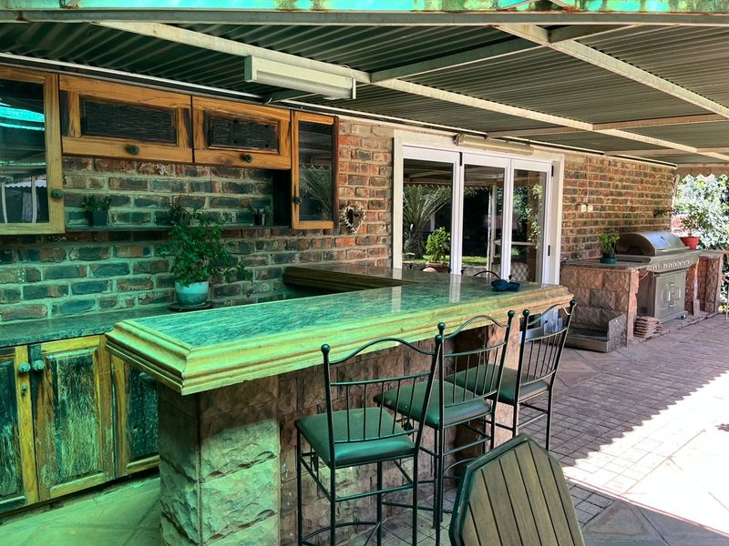 Covered outdoor entertainment area featuring a built-in bar with stone cladding, brick walls, and a built-in braai, perfect for alfresco dining and social gatherings.
