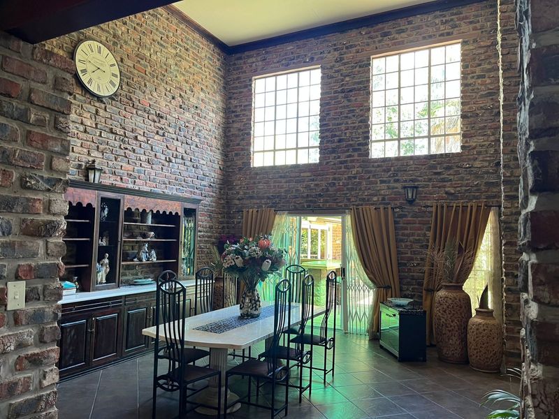 Spacious dining room featuring double volume exposed brick walls, large grid windows, tiled flooring, and built-in wooden cabinetry with direct access to the patio.