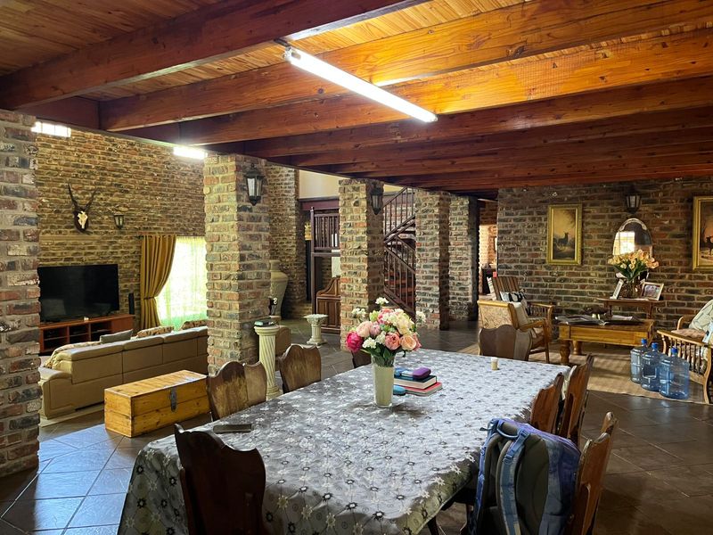 Spacious open-plan living and dining area featuring rustic exposed brick walls, timber beam ceilings, and a spiral staircase.