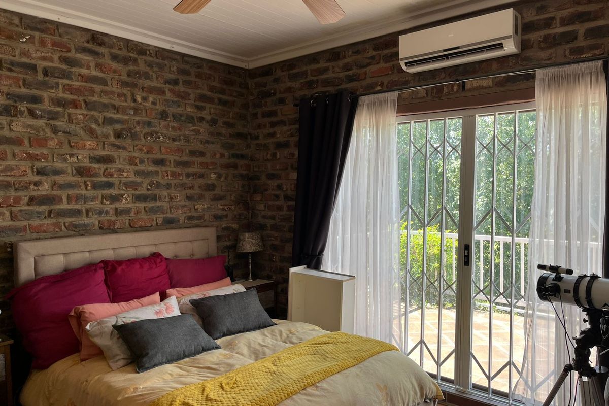 A well-maintained bedroom featuring an exposed brick feature wall, timber ceiling, split-system air conditioning, and direct access to an outdoor patio through sliding doors.
