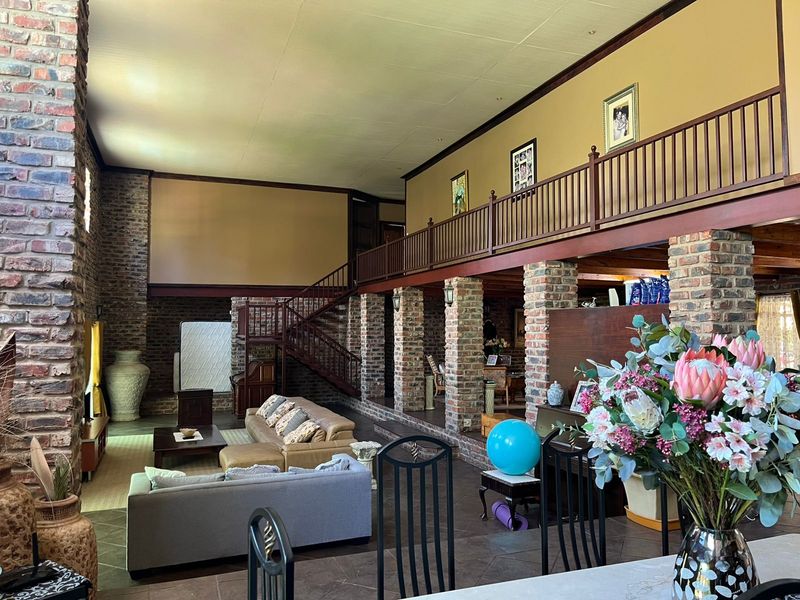 Spacious open-plan living area featuring double-volume ceilings, exposed brick columns, a feature fireplace, and a mezzanine level with a wooden balustrade.