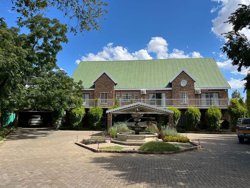Front elevation of a double-story brick residence featuring a green metal roof, paved driveway, central water fountain, and an integrated carport.