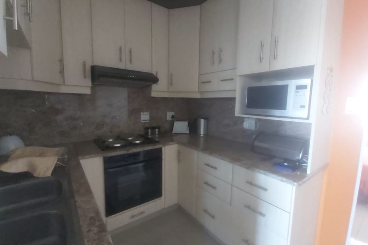 Compact kitchen featuring light-toned cabinetry, stone-look laminate countertops, built-in oven, gas hob, extractor fan, and integrated microwave.
