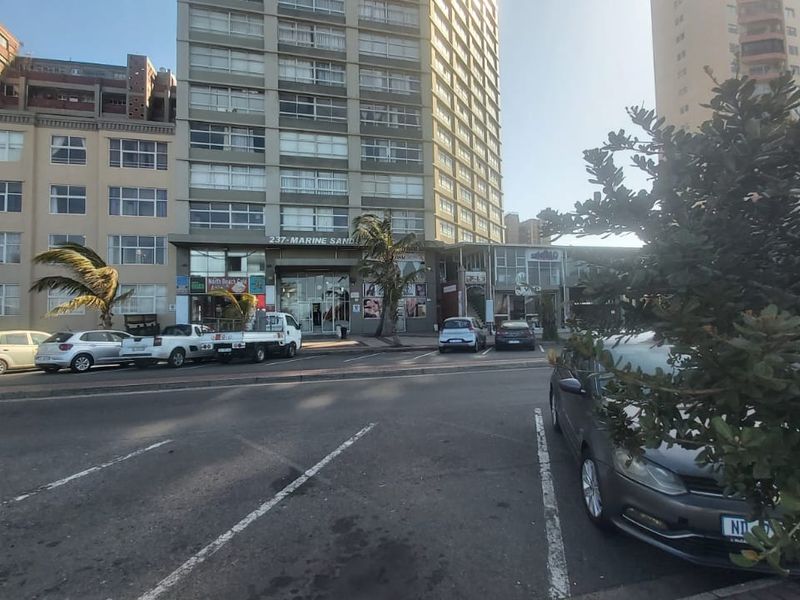 Street-level view of the Marine Sands apartment building, featuring ground-floor commercial spaces and an accessible paved parking area.