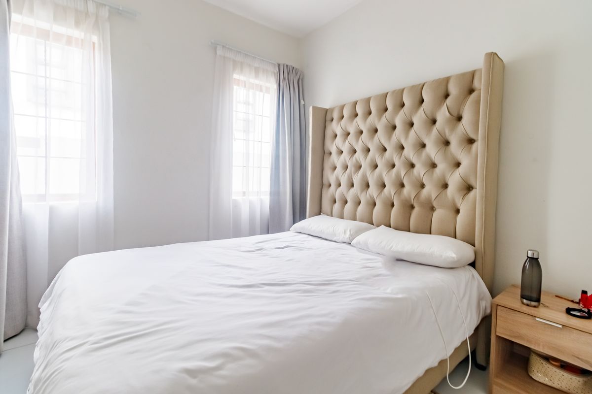 A bright and neutral bedroom featuring tiled flooring and dual windows with installed curtain tracks.
