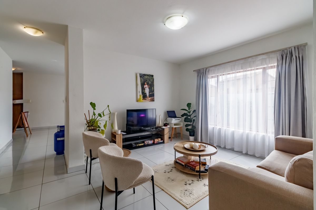 A bright and well-maintained living room featuring neutral tiled flooring and large windows with curtain tracks, offering a clean and functional living space.