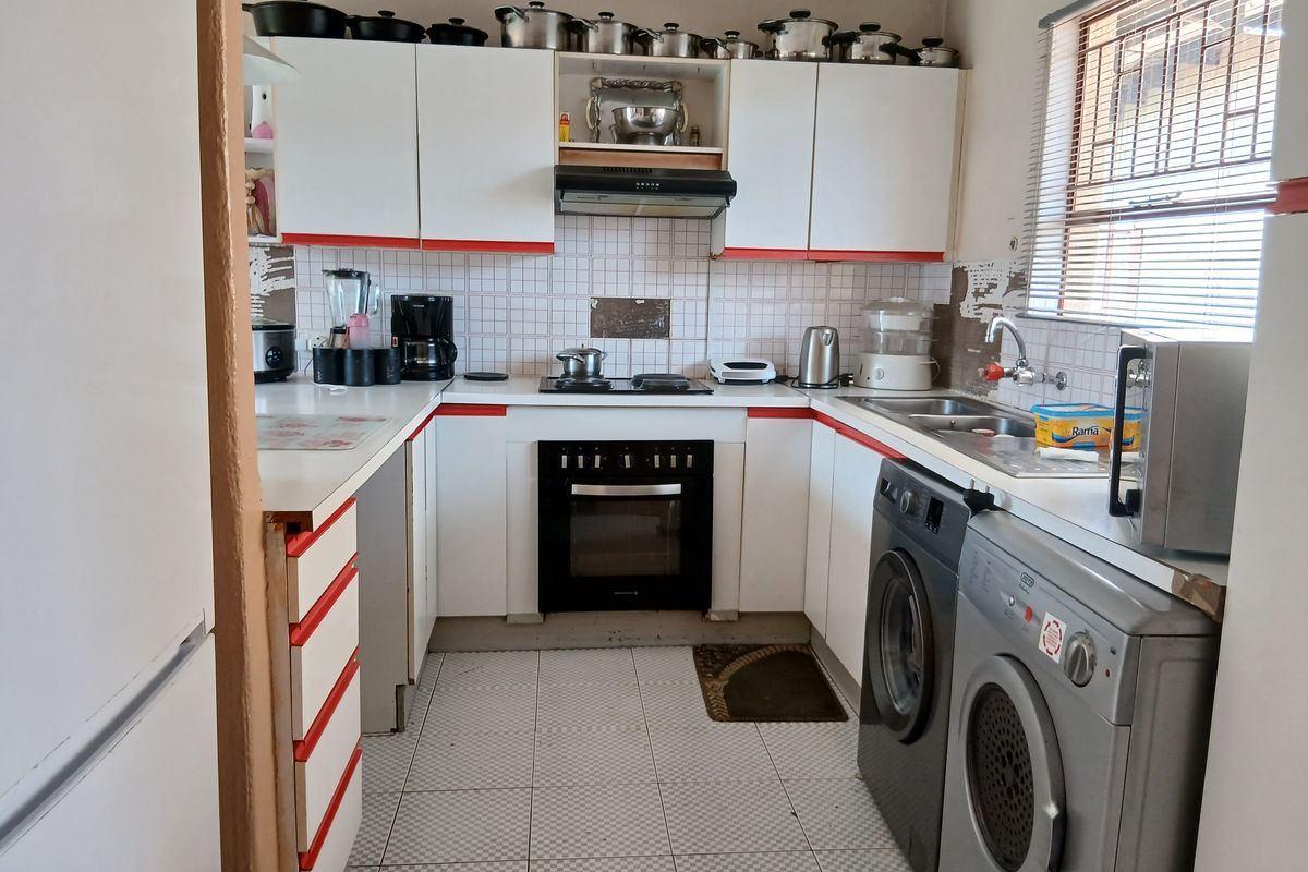 Compact kitchen featuring built-in cabinetry, integrated oven and hob, extractor fan, and dedicated space for laundry appliances under the counter.
