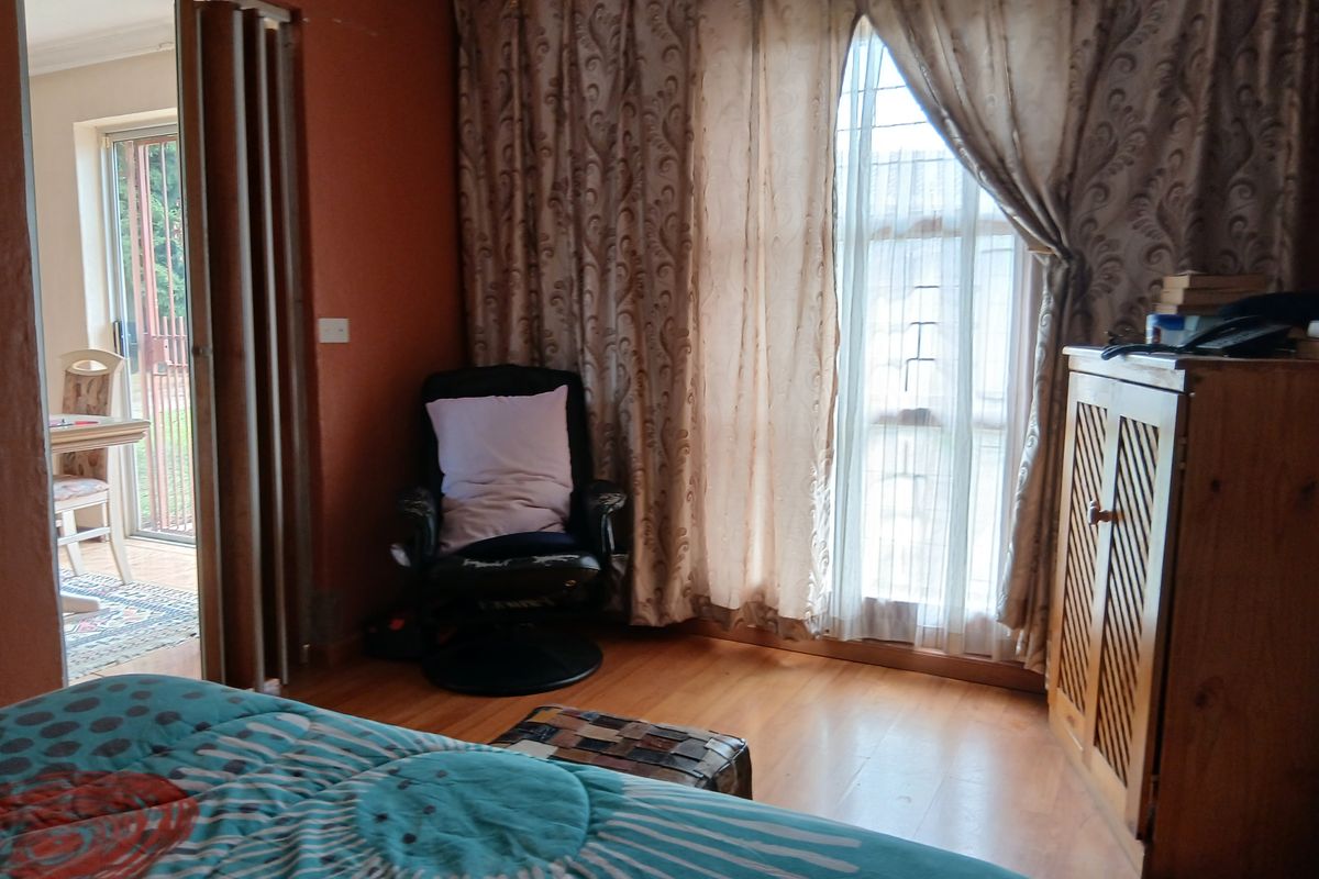 A bedroom featuring laminate wood flooring, large windows with curtains, and a folding door leading to an adjacent patio area.