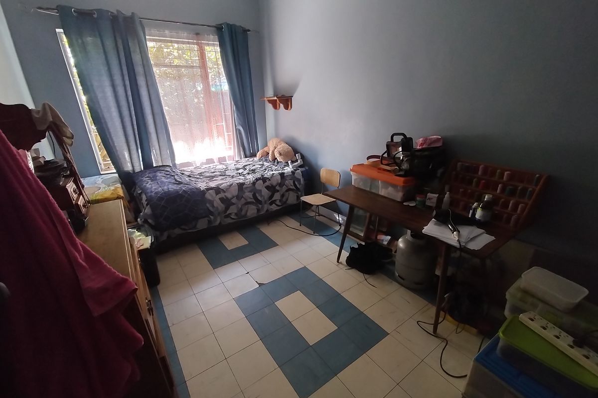 A bedroom featuring tiled flooring with visible cracks, natural light from a window, and curtain rails installed.