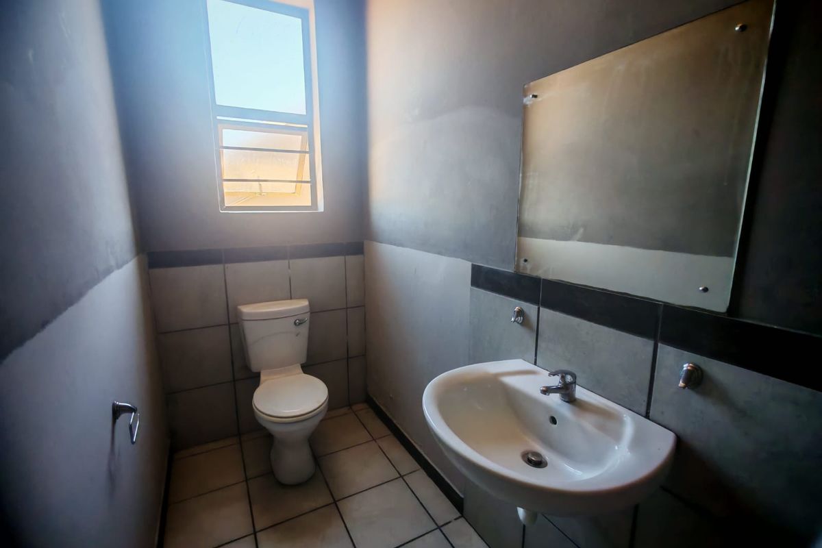 A compact bathroom featuring a wall-mounted basin, toilet, and tiled finishes. The space requires cosmetic updates to the wall surfaces.