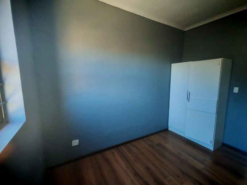 A bedroom featuring dark grey walls, laminate flooring, and a built-in white cupboard.
