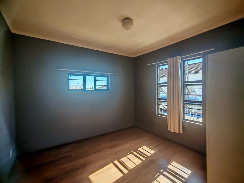 An empty bedroom featuring laminate flooring, dark grey walls, and windows fitted with security burglar bars.