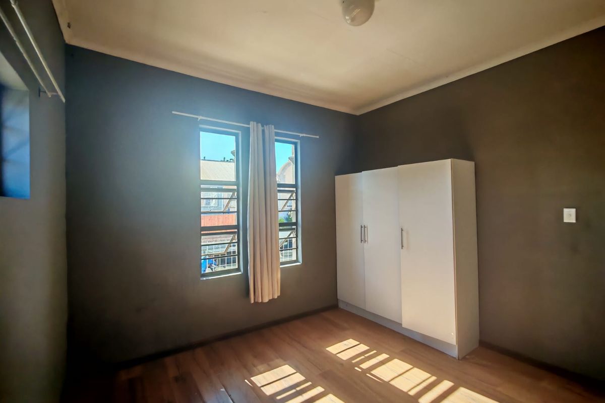 A simple bedroom featuring laminate flooring, dark painted walls, and a built-in wardrobe with security bars on the windows.