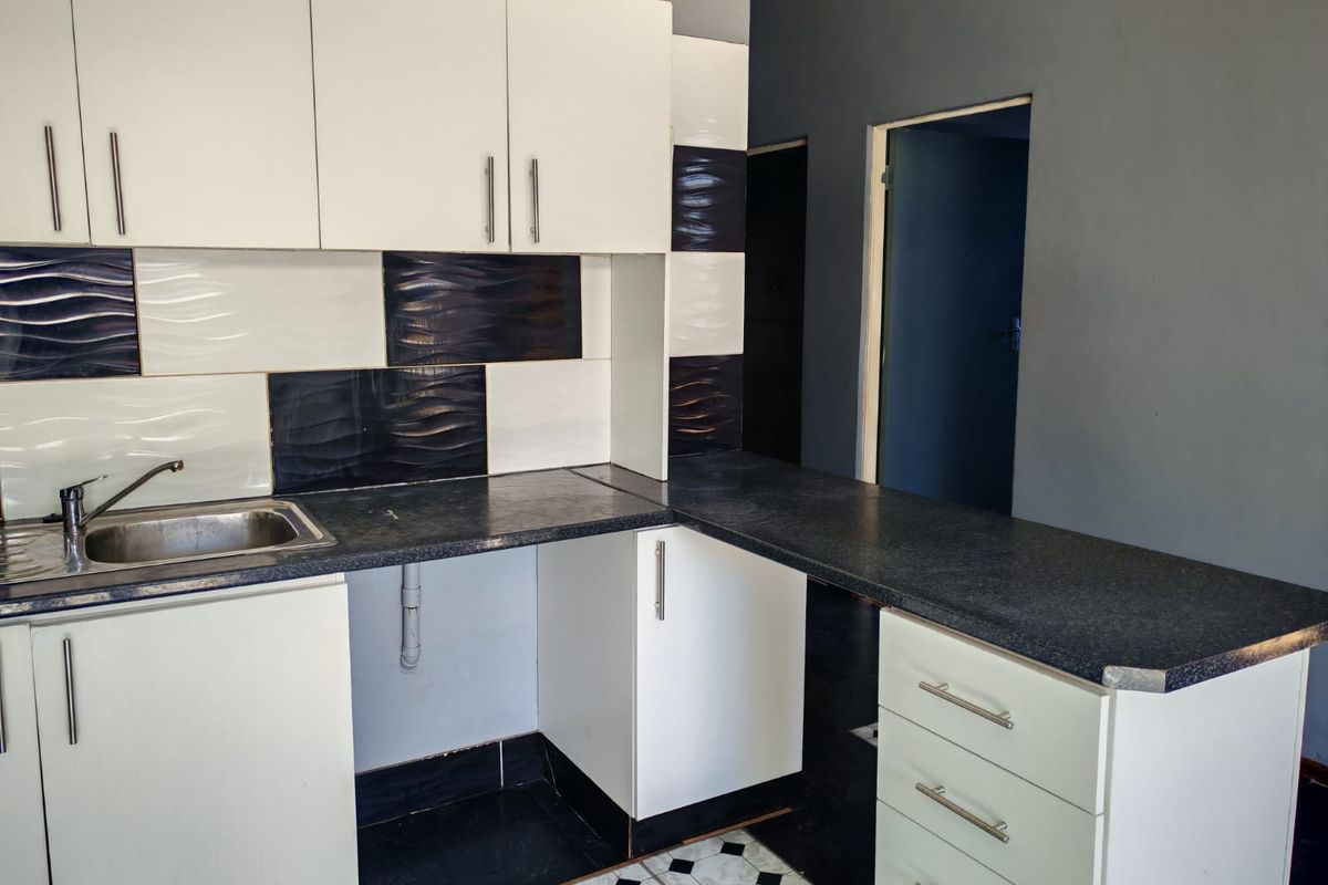 A compact kitchen featuring white cabinetry, dark laminate countertops, a stainless steel sink, and a contrasting black and white tiled backsplash.