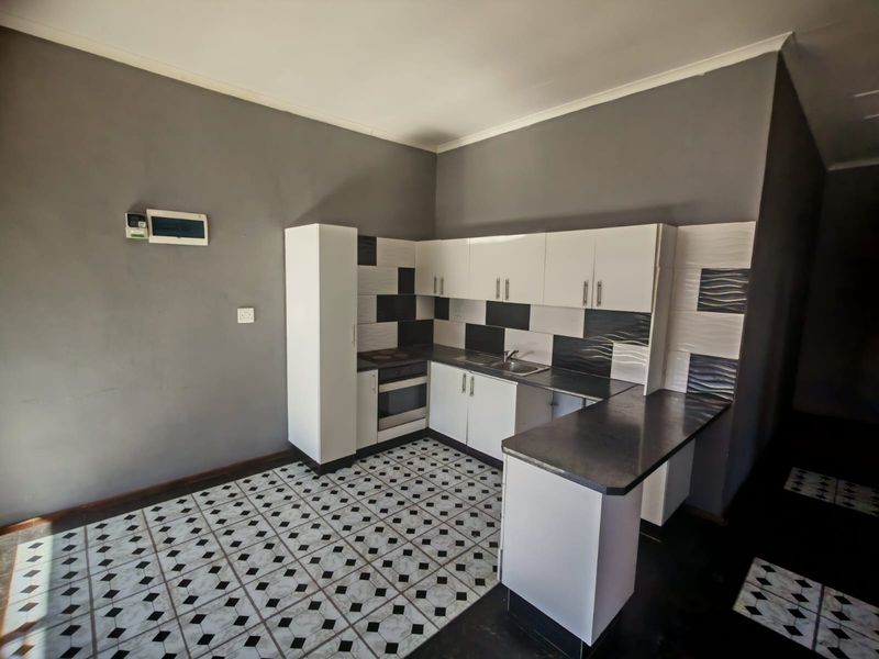 A compact kitchen featuring white cabinetry, dark laminate countertops, a built-in oven, and a distinctive patterned tiled floor.