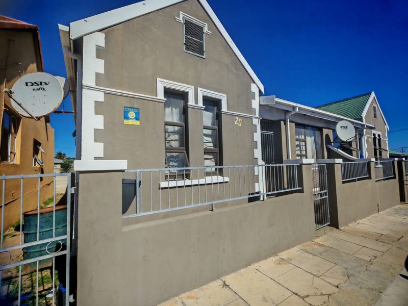 Front elevation of a residential property featuring a gabled roof, perimeter wall with metal security gate, and security bars on windows.
