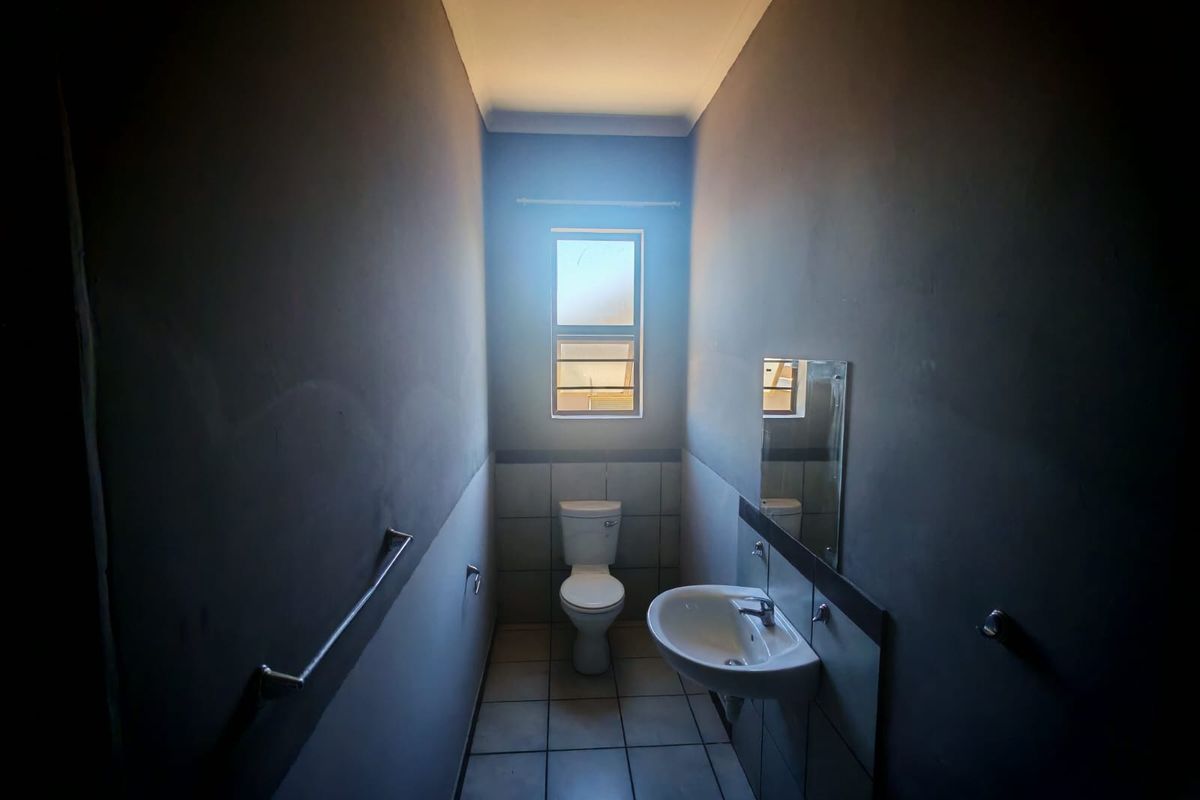 A compact bathroom featuring a pedestal basin, toilet, and tiled flooring, finished with dark wall paint and a window for natural light.