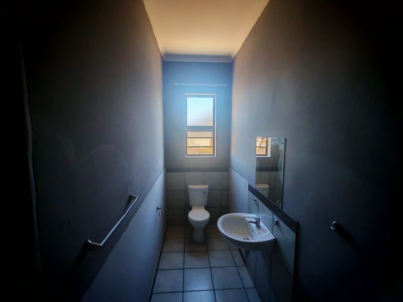 A compact bathroom featuring a pedestal basin, toilet, and tiled flooring, finished with dark wall paint and a window for natural light.
