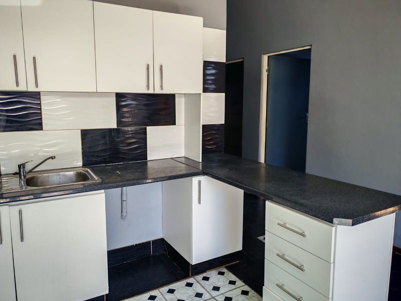 A compact kitchen featuring white cabinetry, dark laminate countertops, a stainless steel sink, and a contrasting black and white tiled backsplash.