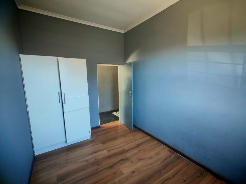 A vacant bedroom featuring laminate flooring, a built-in wardrobe, and grey painted walls.