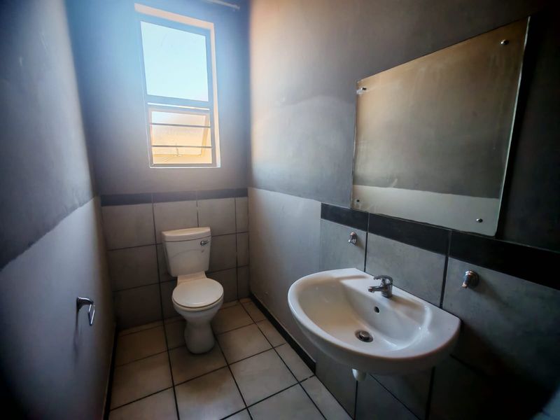 A compact bathroom featuring a wall-mounted basin, toilet, and tiled finishes. The space requires cosmetic updates to the wall surfaces.