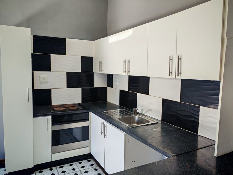 A compact kitchen featuring white cabinetry, dark laminate countertops, a built-in oven with electric hob, and a distinctive black and white checkered tiled backsplash.