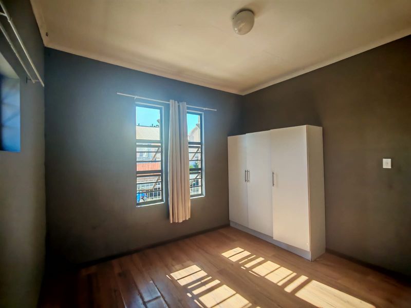 A simple bedroom featuring laminate flooring, dark painted walls, and a built-in wardrobe with security bars on the windows.