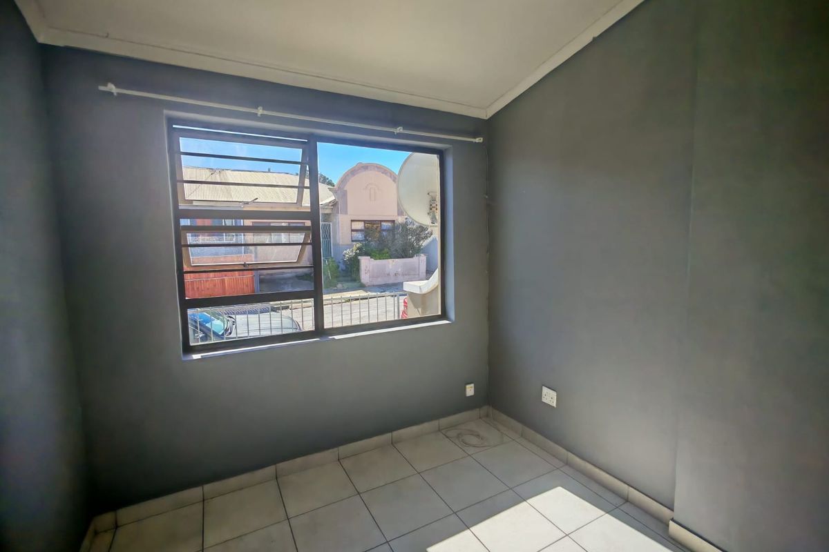 An empty bedroom featuring tiled flooring, grey painted walls, and a window fitted with security bars.