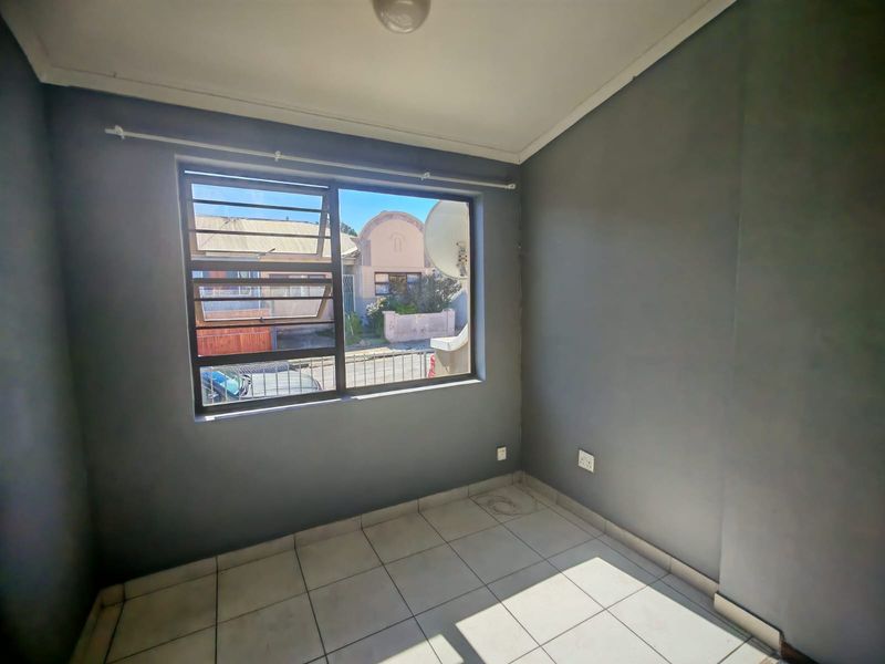 An empty bedroom featuring tiled flooring, grey painted walls, and a window fitted with security bars.
