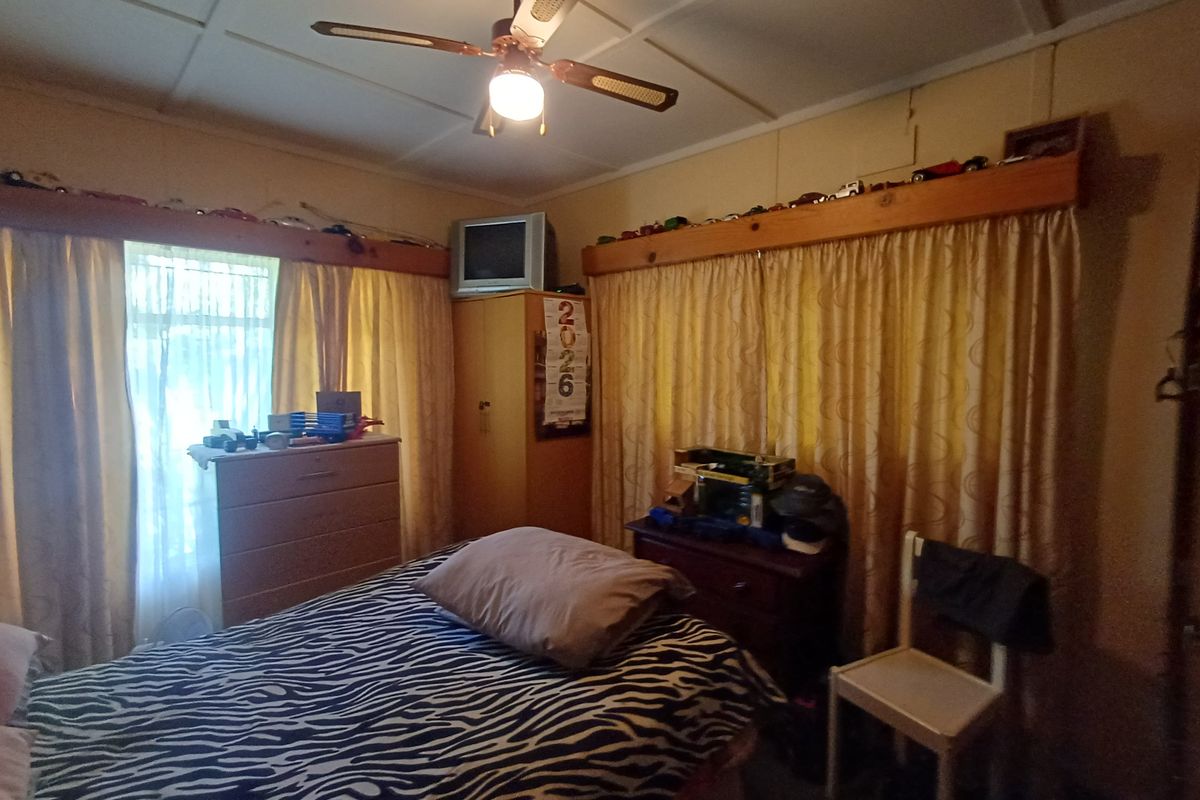 A bedroom featuring a ceiling fan, timber-framed window treatments, and basic wall finishes, requiring cosmetic updates to modernize the space.