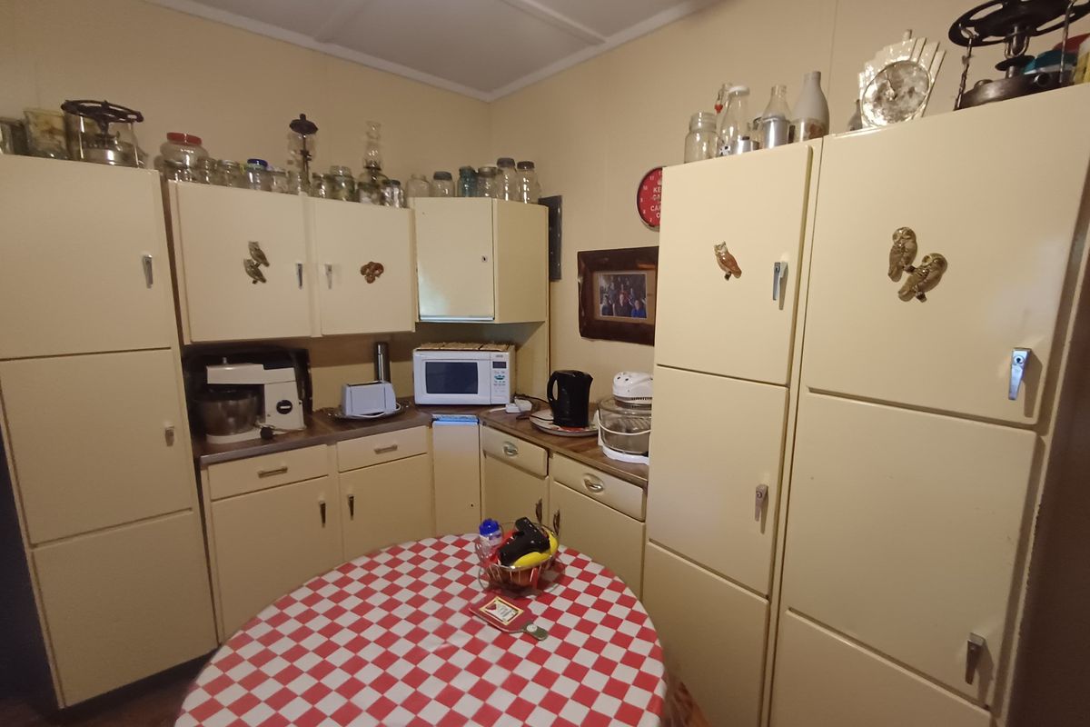 A compact, dated kitchen featuring original cabinetry, laminate countertops, and built-in storage units, offering potential for a modern renovation.