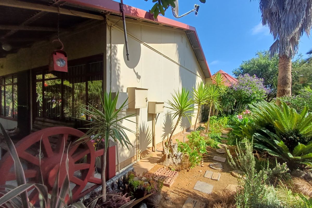 A side view of the property featuring a covered patio area, established garden landscaping, and a paved walkway along the exterior wall.