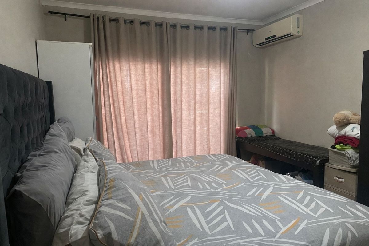 A functional bedroom featuring a wall-mounted split-system air conditioner and a sliding door with curtain treatments.