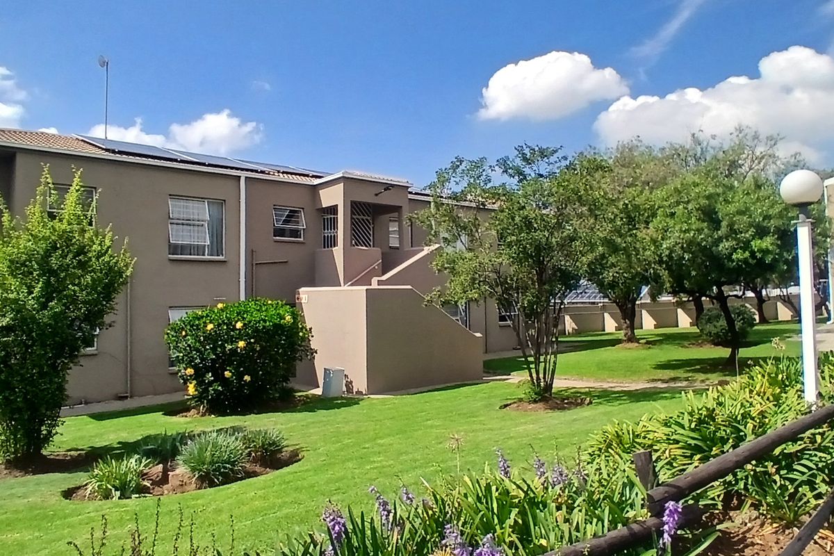 Exterior view of a townhouse complex featuring well-maintained communal gardens, paved walkways, and multi-story residential units with solar panels.