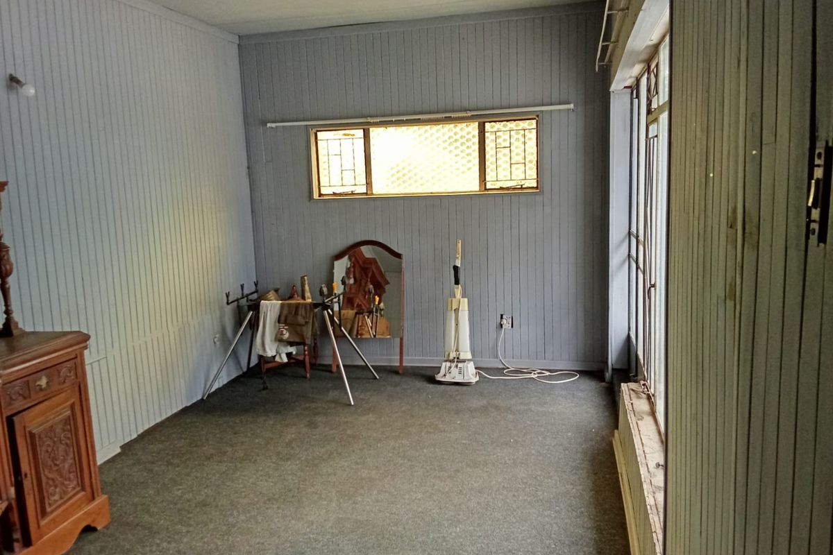 A spacious bedroom featuring timber wall paneling, carpet flooring, and large windows with security bars, offering a blank canvas for renovation.