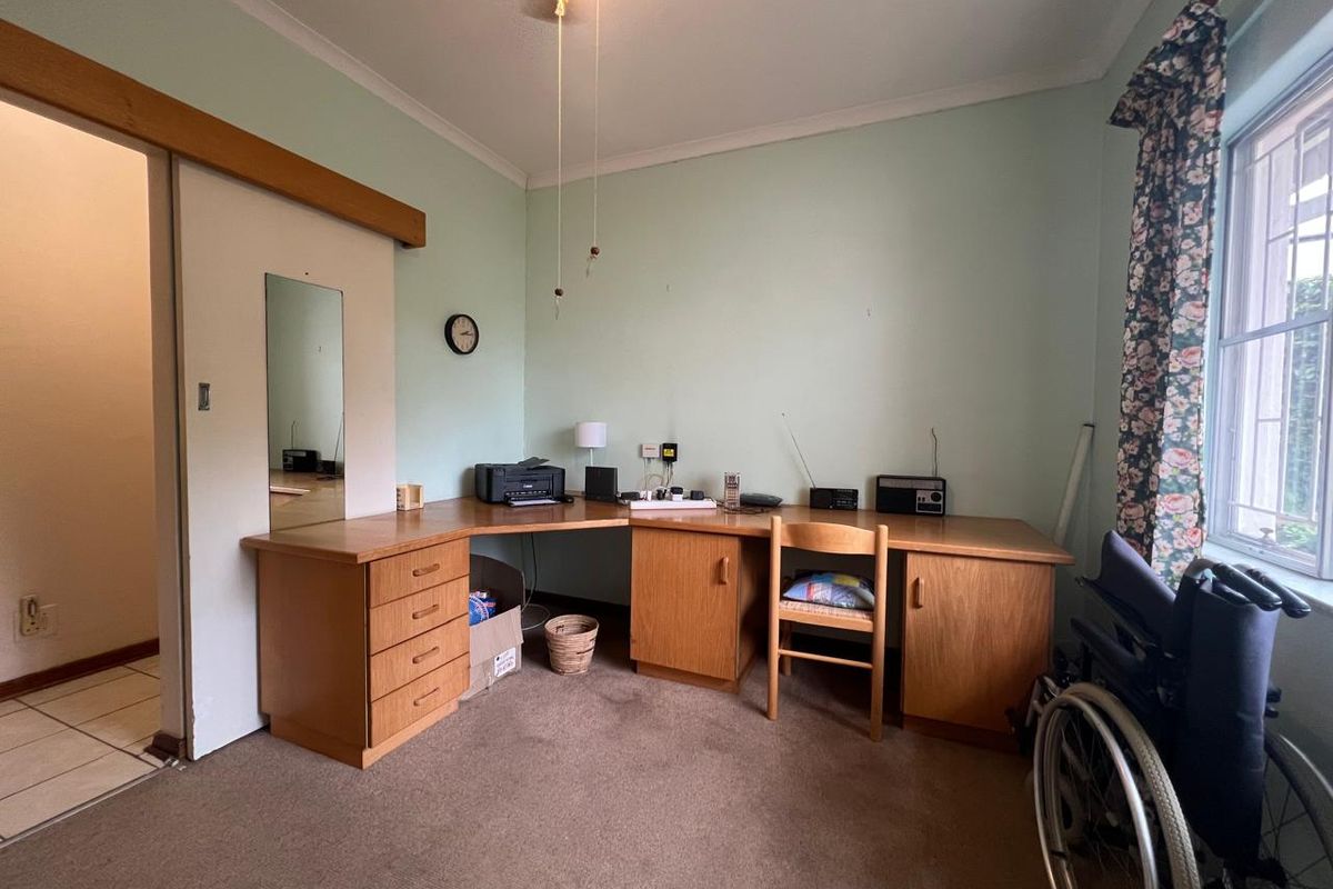 A bedroom featuring a built-in wooden desk unit, sliding door access, and security bars on the window.