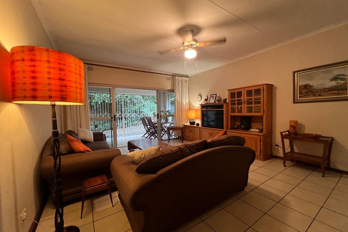 A comfortable living room featuring tiled flooring, a ceiling fan, and large sliding glass doors that provide access to an outdoor patio area.
