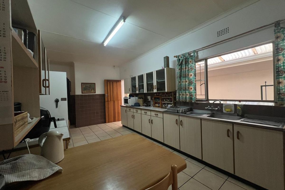 A functional kitchen featuring extensive built-in cabinetry, laminate countertops, a double stainless steel sink, and tiled flooring with a neutral color palette.