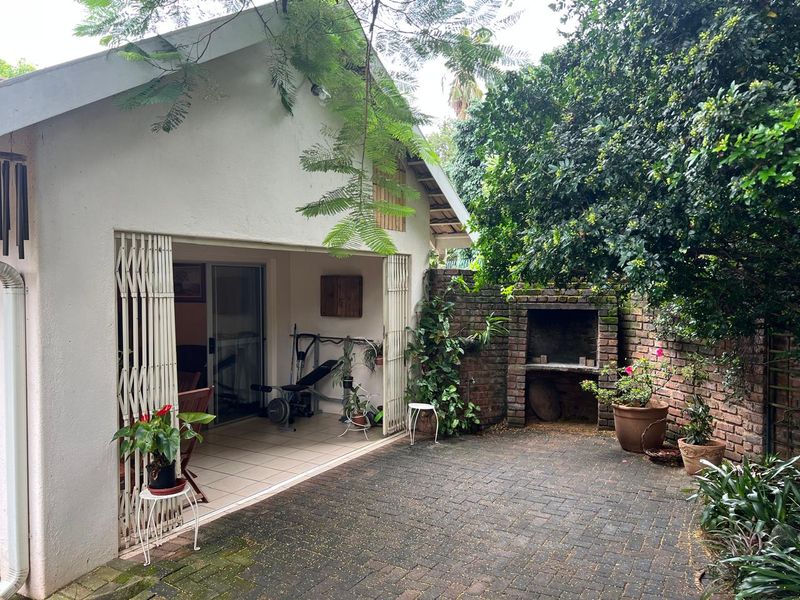 Covered patio area featuring a built-in brick braai, tiled flooring, and direct access to the garden through sliding security gates.