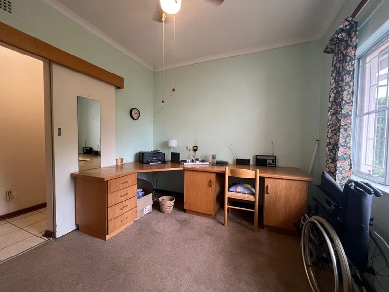 A bedroom featuring a built-in wooden desk unit, sliding door access, and security bars on the window.